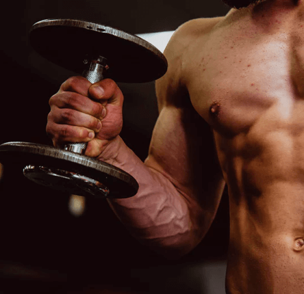 Eine hemdsärmelige Person hebt eine Hantel mit einer Hand und zeigt dabei definierte Arm- und Brustmuskeln. Der Hintergrund des Fitnessstudios ist unscharf und konzentriert sich auf den muskulösen Oberkörper der Person und den starken Griff nach dem Gewicht.